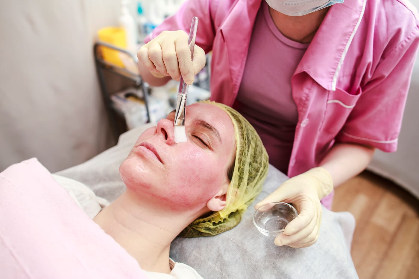Kosmetička nanáší štětcem chemický peeling na pleť klientky