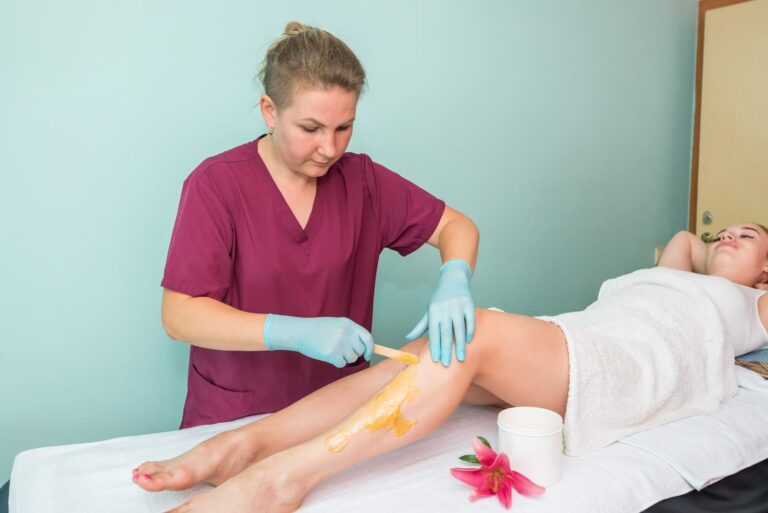 Depilace cukrovou pastou — kosmetička nanáší sugaring pastu dřevěnou špachtlí
